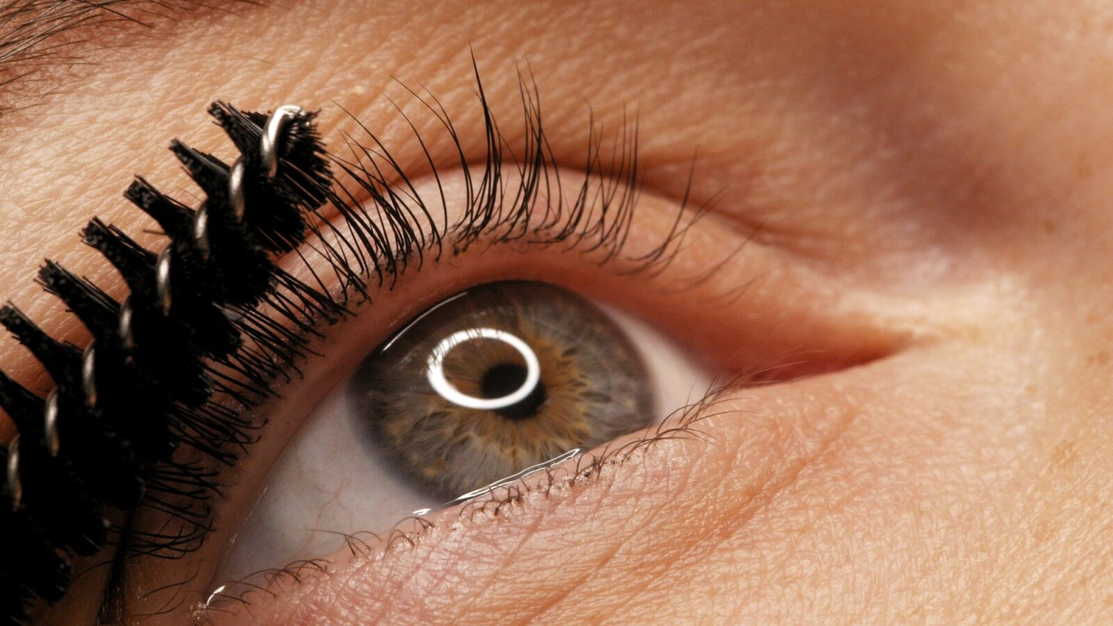 Applying black mascara to the eyelashes with a makeup brush. Applying makeup in a beauty salon.