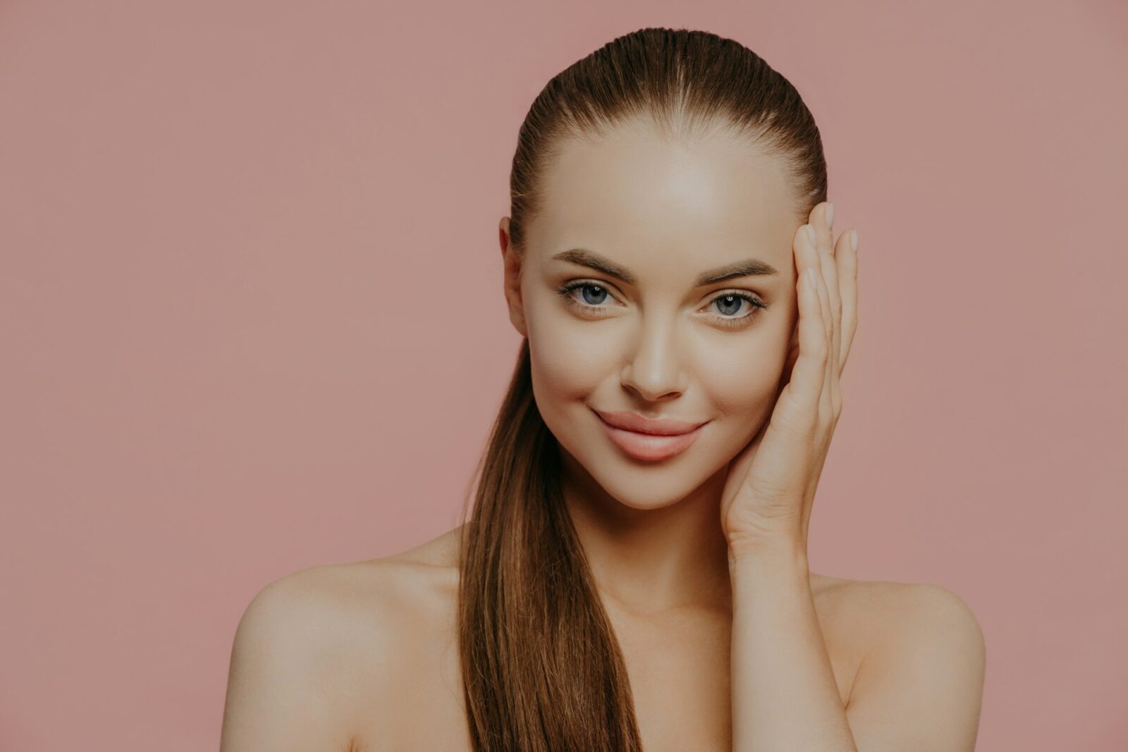Isolated shot of pretty woman with combed pony tail, enjoys freshness of skin